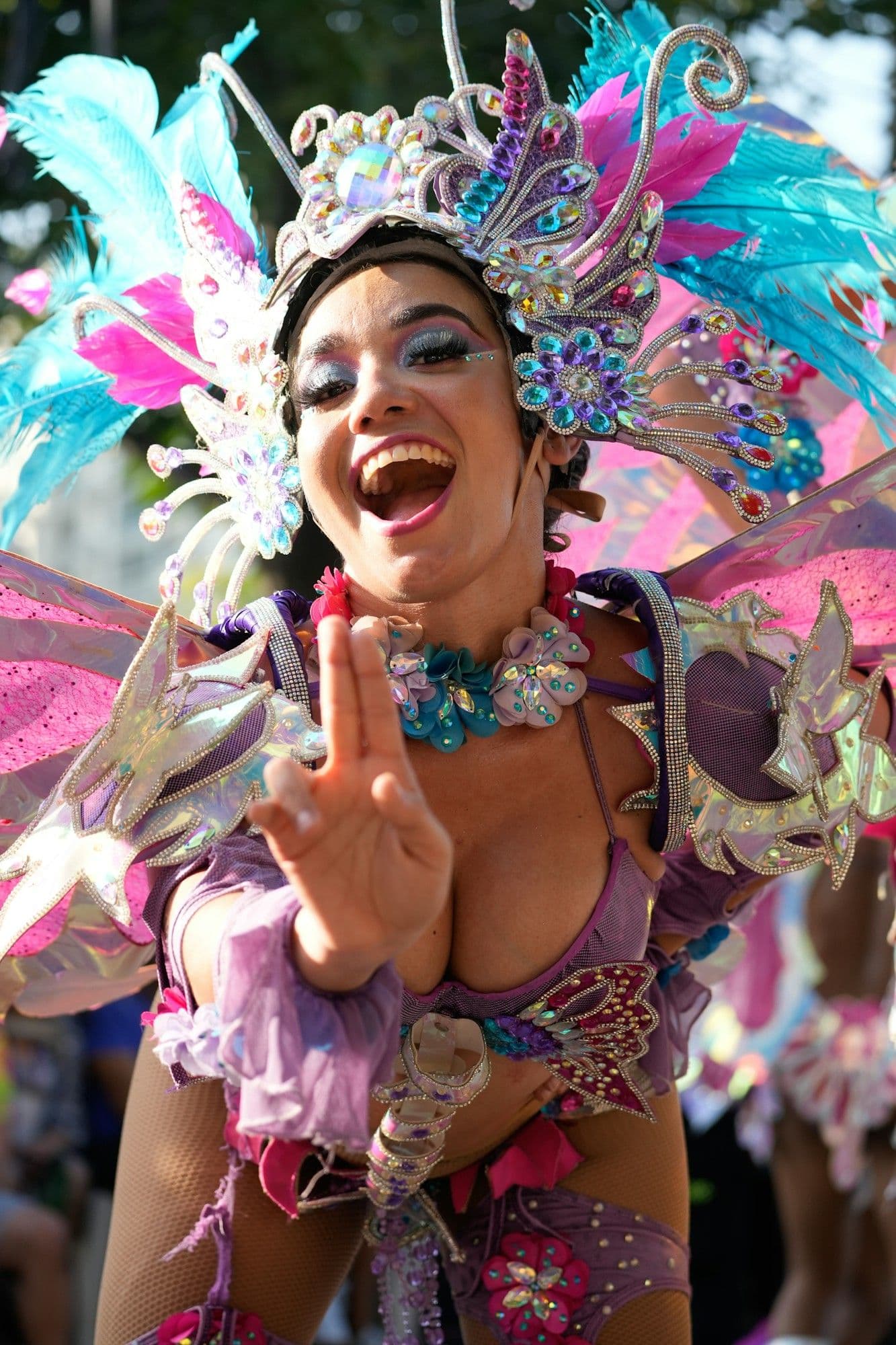 Una sonriente reina del Carnaval de Barranquilla con un tocado de plumas rosado y turquesa hace el signo de paz