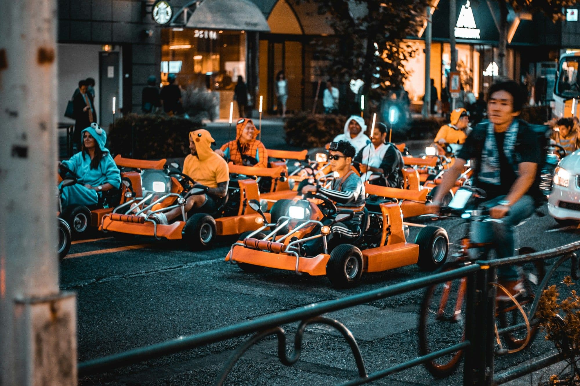 Conductores disfrazados en karts naranja brillante alineados en una calle de la ciudad de noche