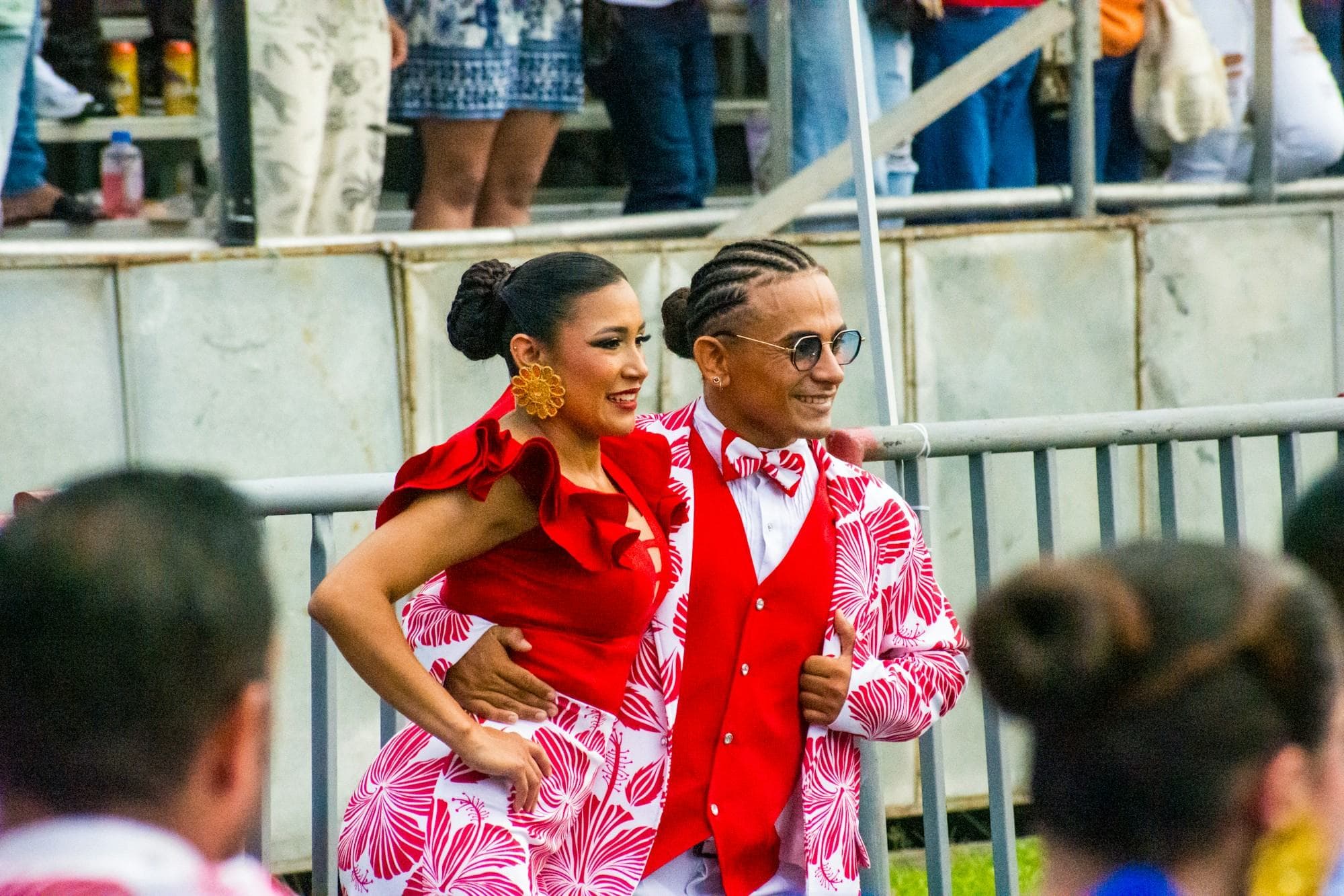 Una sonriente pareja de salsa vestida de rojo y rosado baila en el desfile de la Feria de Cali mientras el público mira