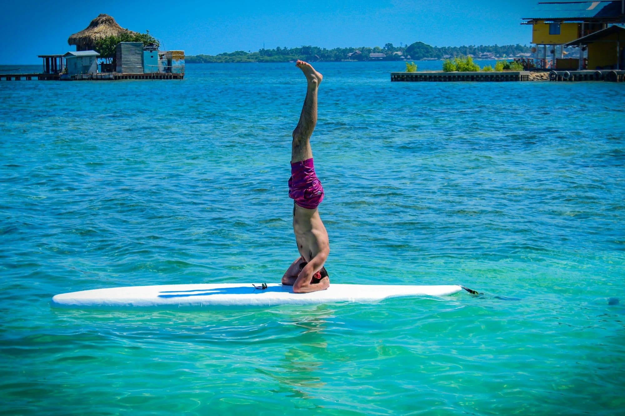 Un viajero hace una parada de manos sobre una tabla de paddle en el agua turquesa y cristalina del Caribe en las islas de San Bernardo