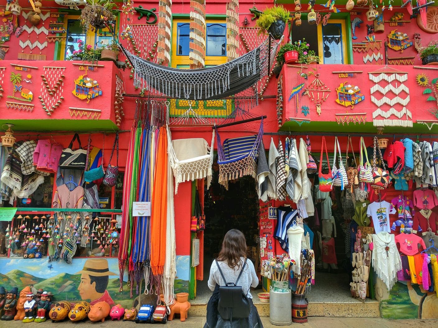 A traveler browses a bright red craft shop in Ráquira draped with hammocks, bags and pottery