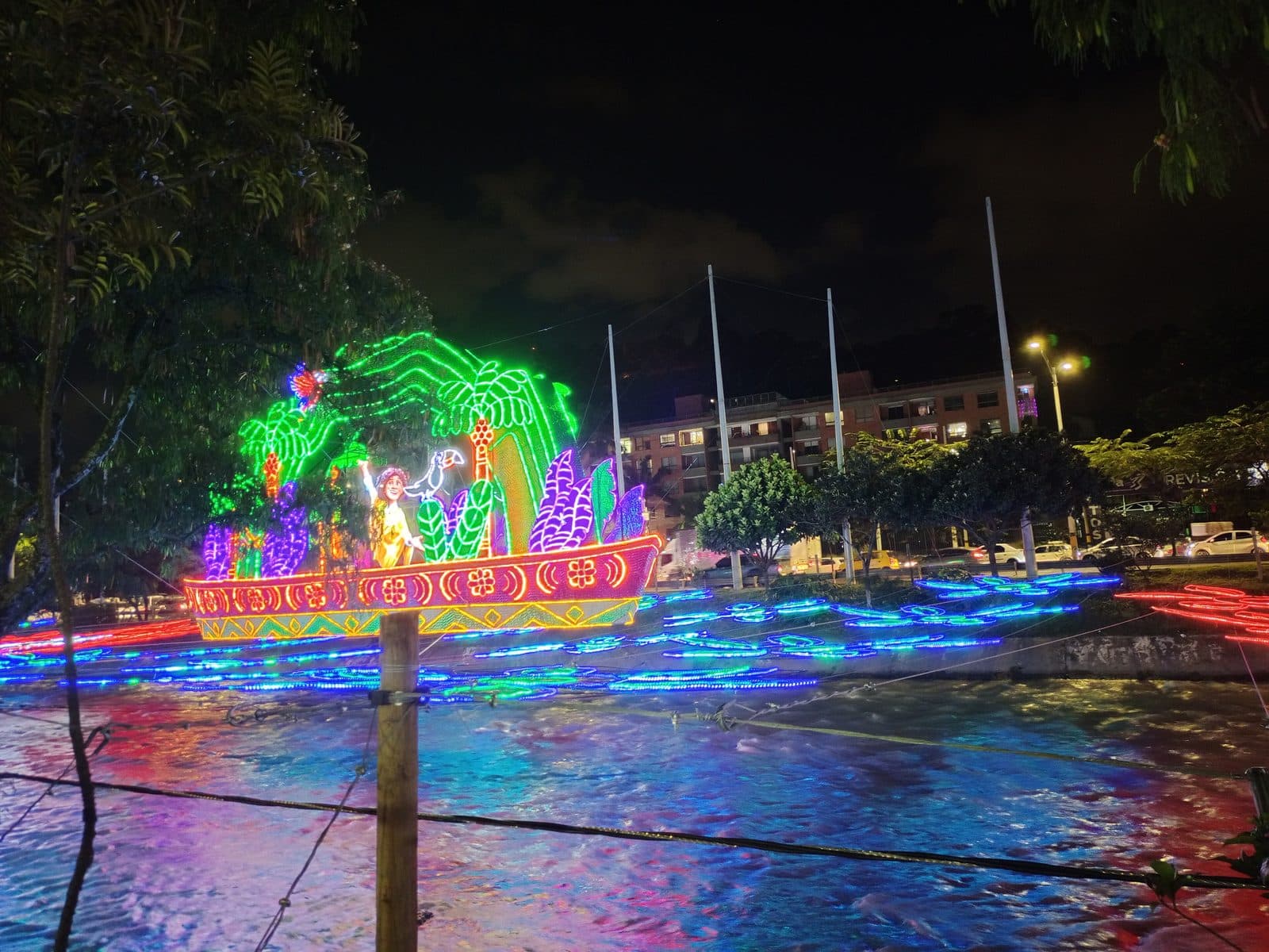 Medellín's Christmas lights glowing in rainbow colors over the river at Parques del Río at night