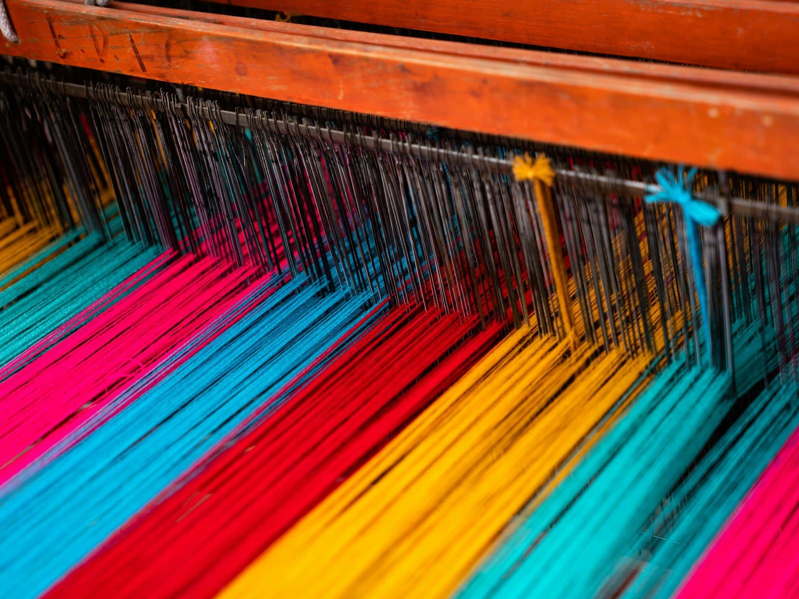 Vivid pink, turquoise, yellow and red threads stretched across a wooden weaving loom