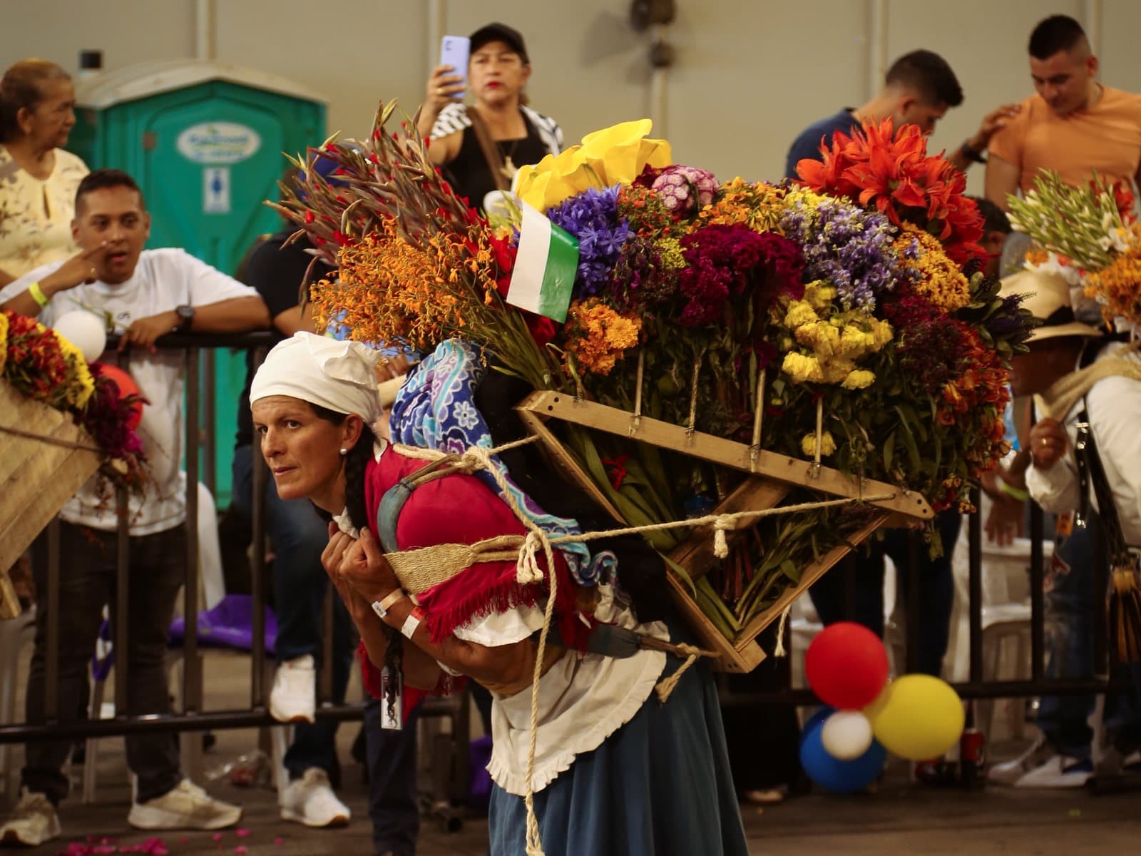 A silletera in traditional dress carries a towering silleta of bright flowers in Medellín