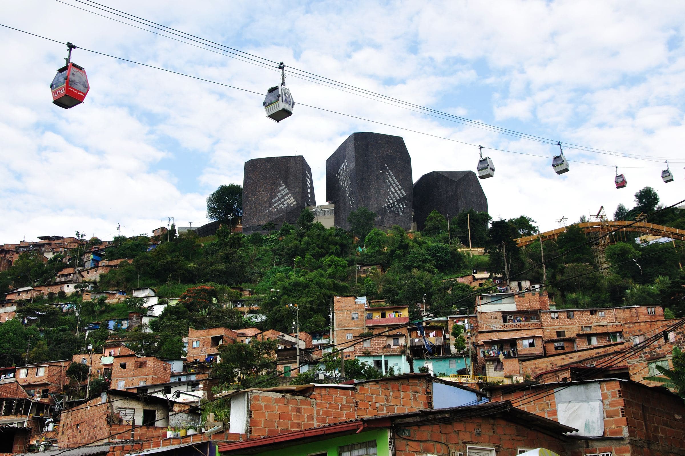 Red Metrocable cabins pass over hillside homes toward Parque Biblioteca España