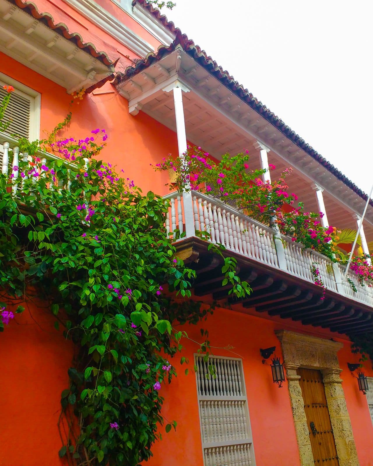 Casa colonial color coral con un balcón blanco cubierto de buganvilias rosadas en Cartagena