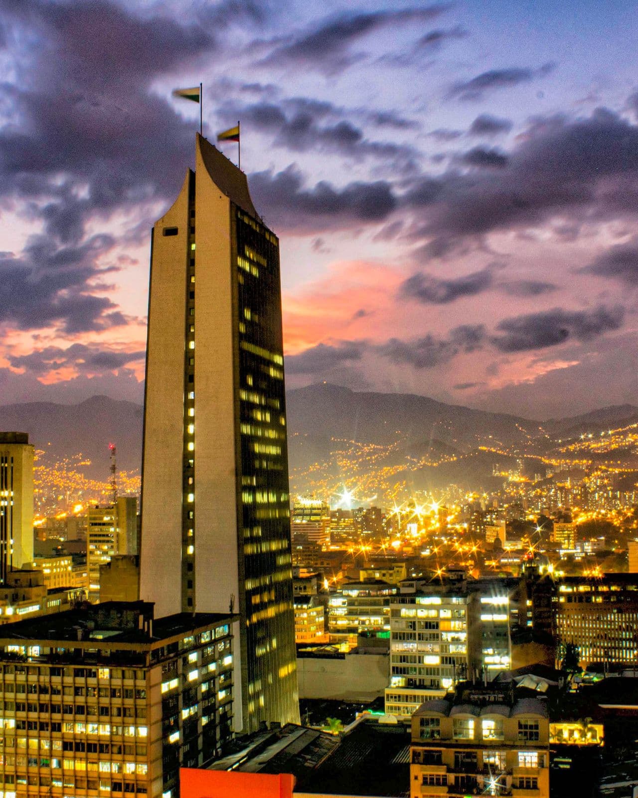 La torre Coltejer y las luces del centro de Medellín bajo un cielo rosado y violeta al atardecer