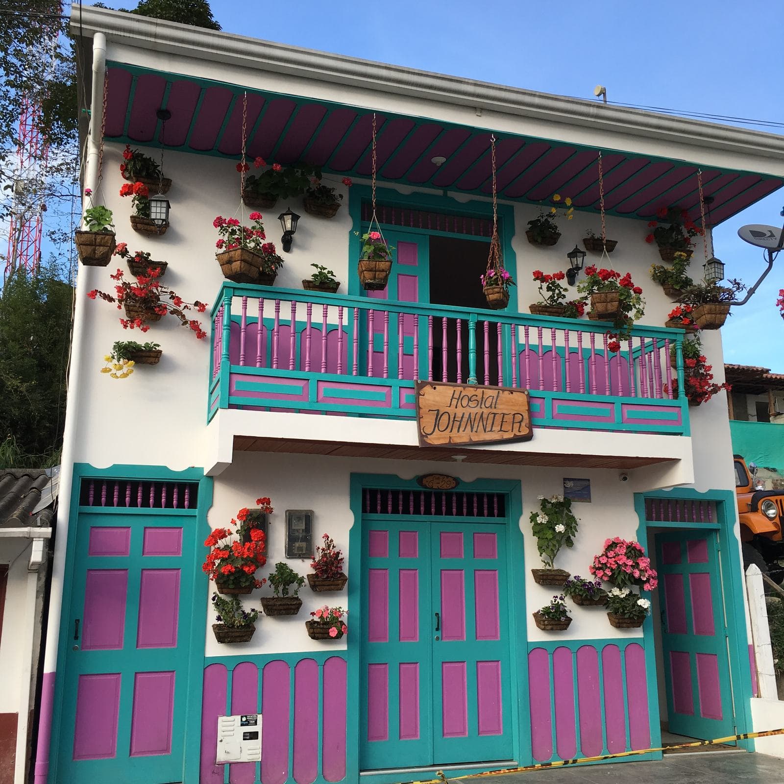 Puertas turquesa y magenta y materas colgantes con flores en una casa tradicional de Salento