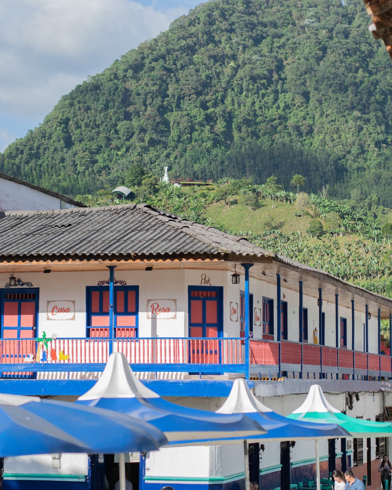 Edificio colonial blanco con puertas rojas y balcón azul bajo montañas verdes en Jardín