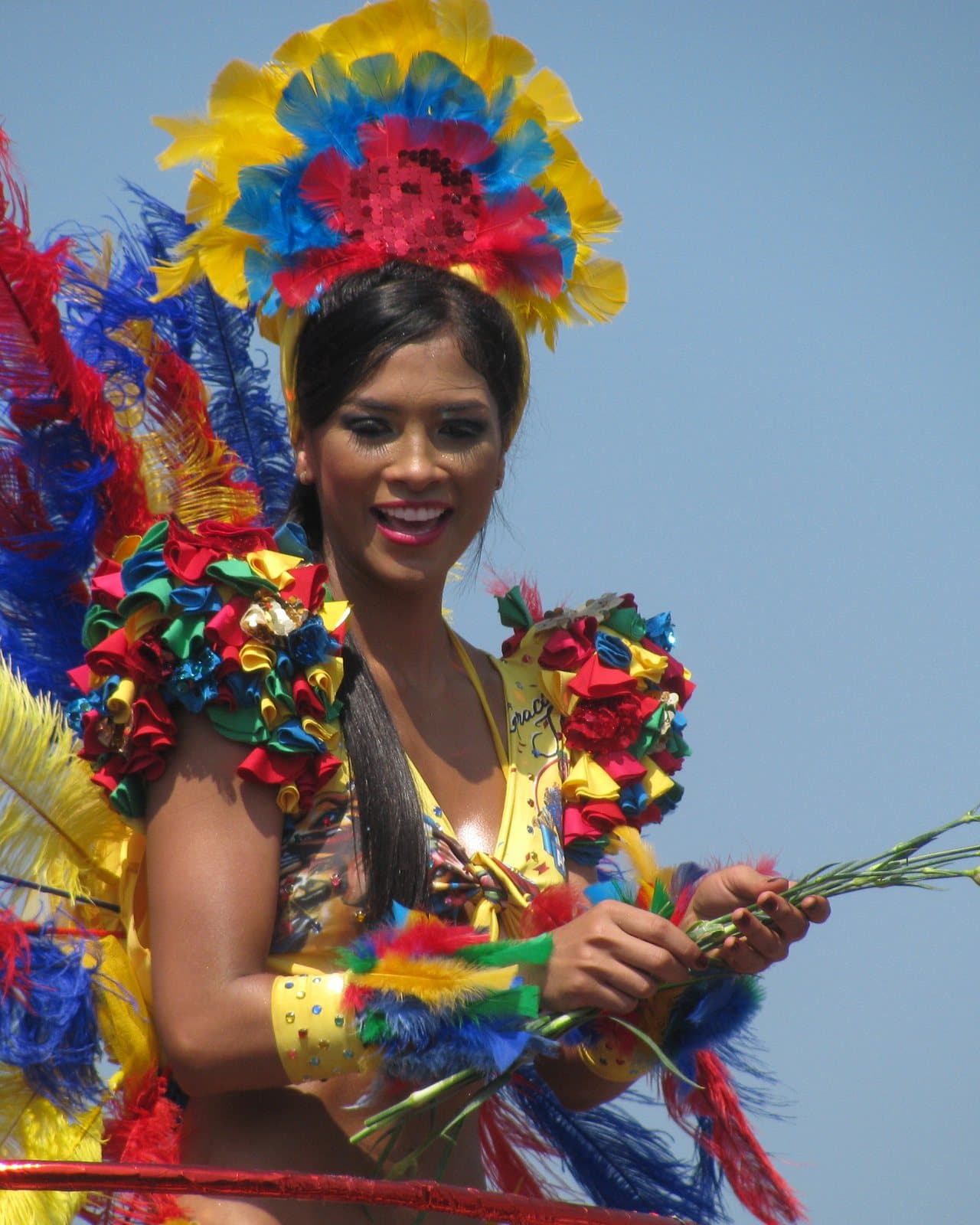 Bailarina sonriente del Carnaval de Barranquilla con un tocado de plumas amarillas, azules y rojas