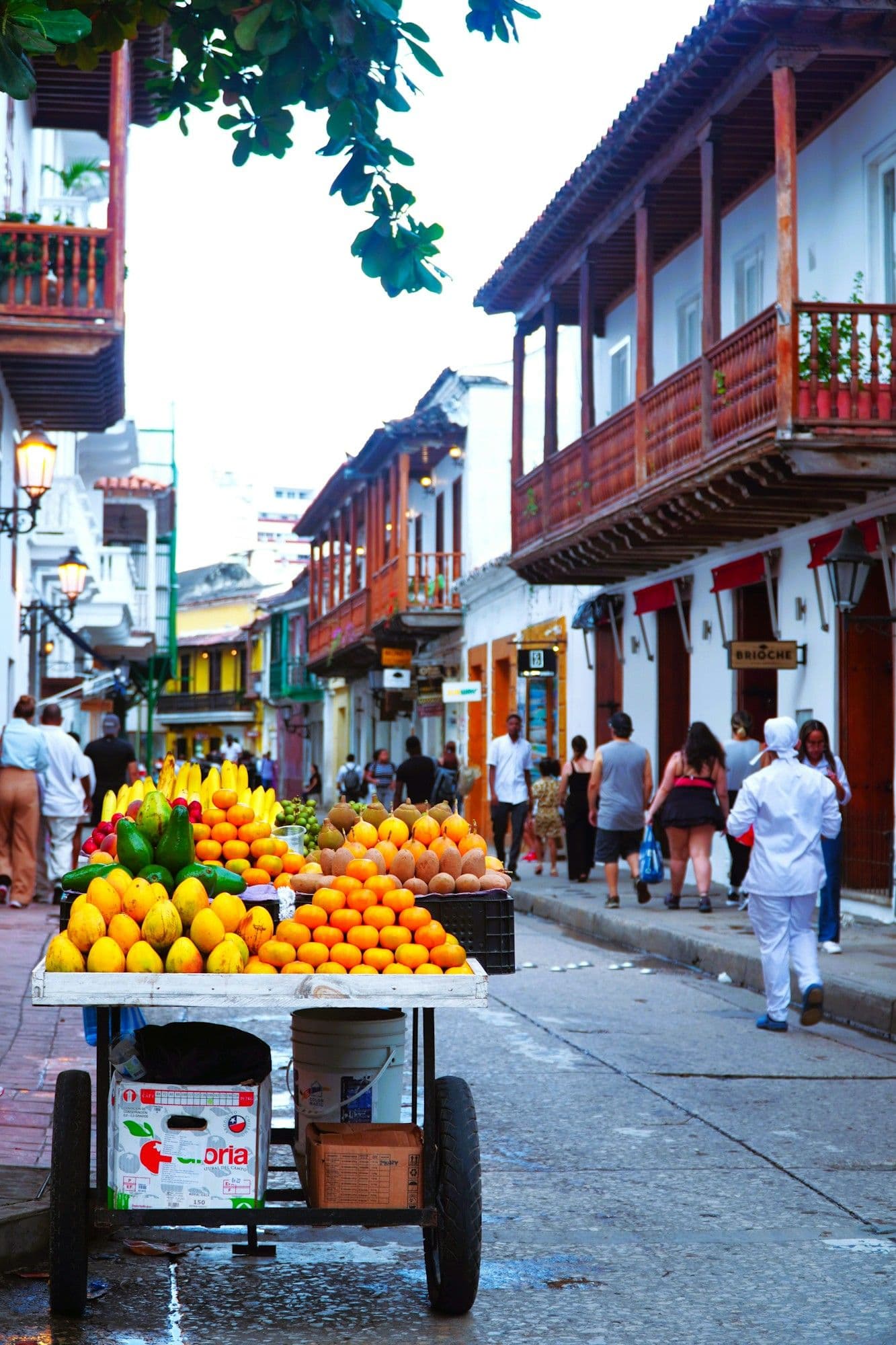 Un carrito de frutas repleto de mangos, naranjas y papayas en una soleada calle colonial de Cartagena