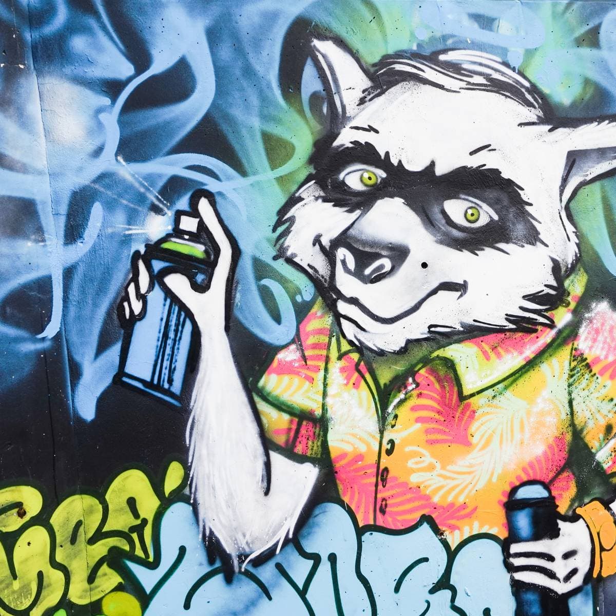 Vivid graffiti mural of a grinning raccoon in a tropical shirt holding a spray can