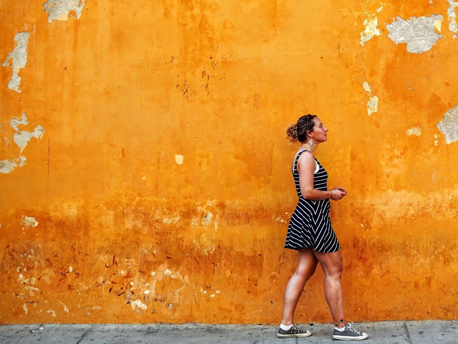 Viajera con vestido de rayas pasea junto a un muro colonial naranja desteñido por el sol en Cartagena