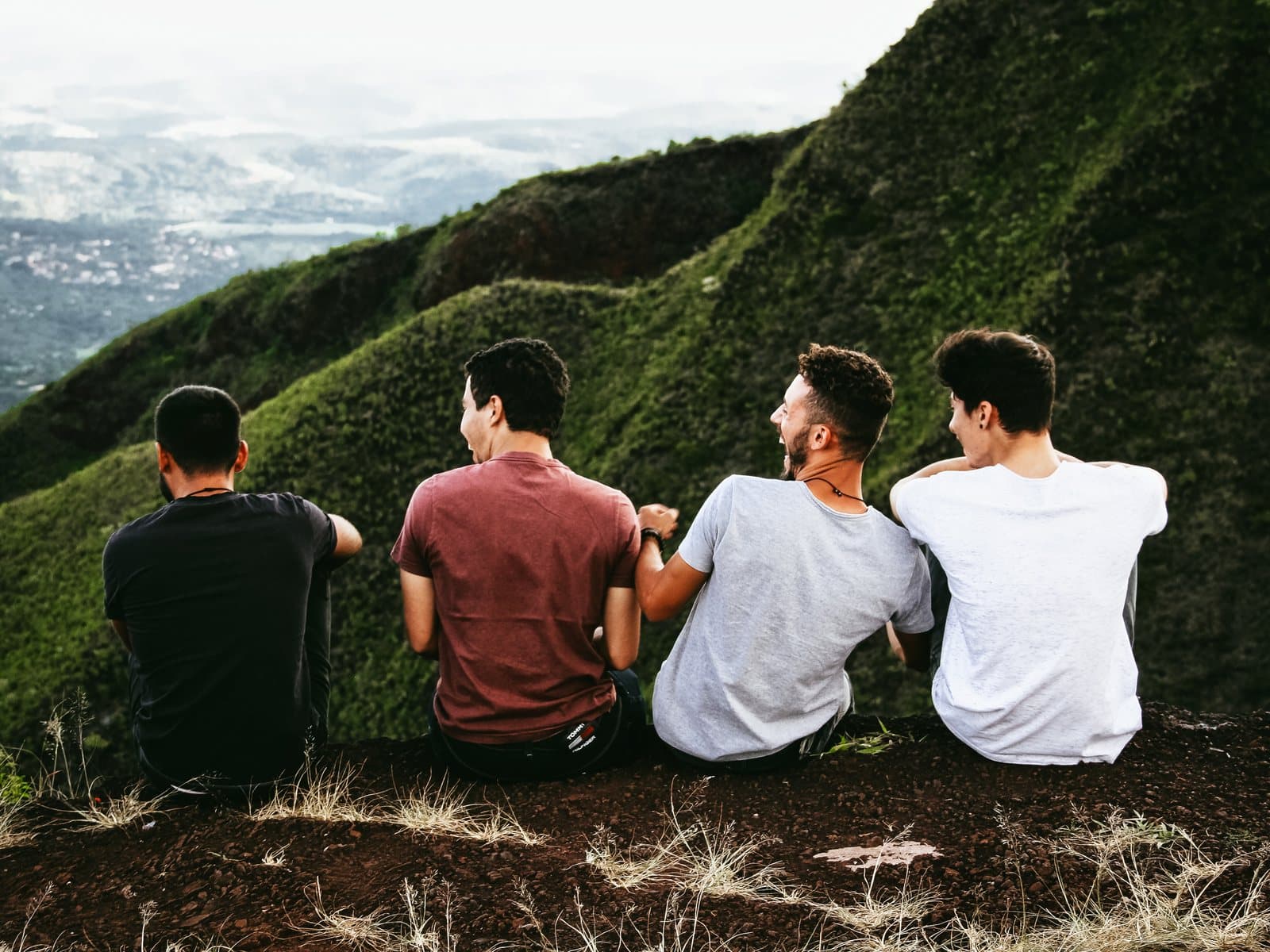Cuatro amigos se ríen juntos en una ladera verde con vista a un amplio valle