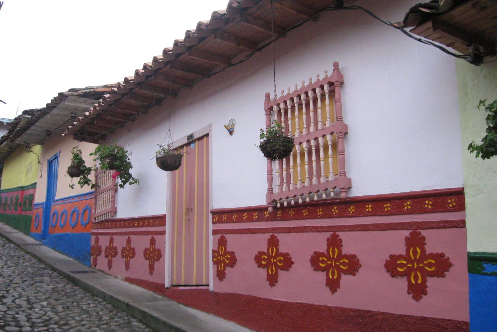 Whitewashed house with a carved wooden door and red painted zócalo panels on a cobbled street