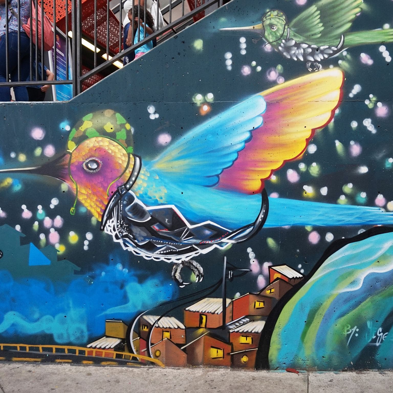 A rainbow-winged hummingbird mural glowing with dots of color on a street wall in Comuna 13