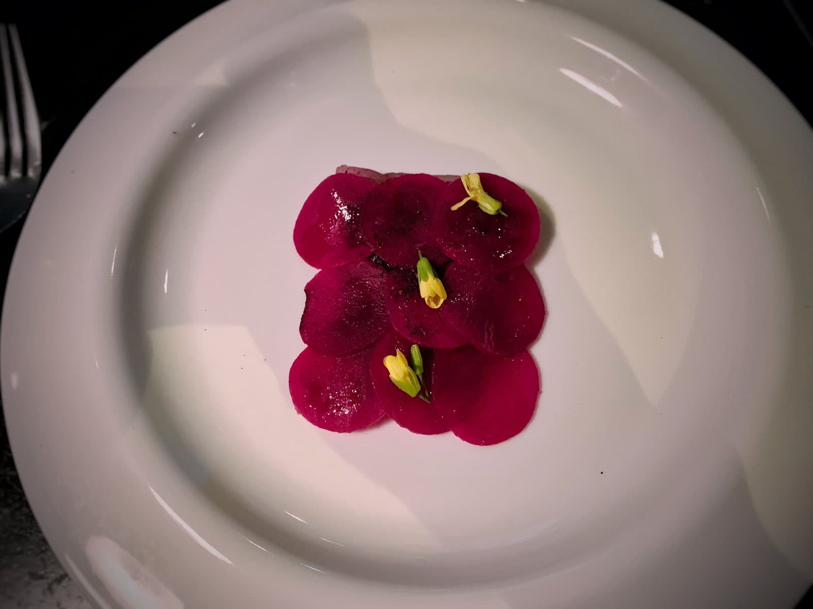 Thin magenta beet carpaccio dotted with yellow flowers on a white plate at Carmen restaurant, Medellín