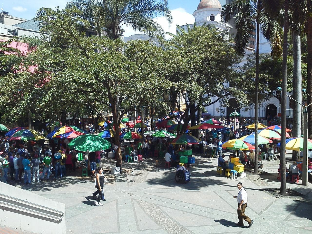 Sombrillas coloridas de vendedores bajo palmas y árboles en el Parque Berrío, centro de Medellín