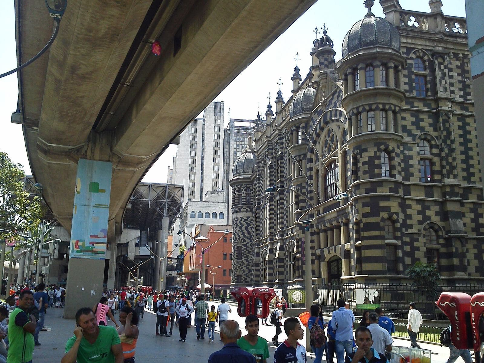 Multitudes caminando bajo el viaducto del metro junto al ajedrezado Palacio de la Cultura en El Centro