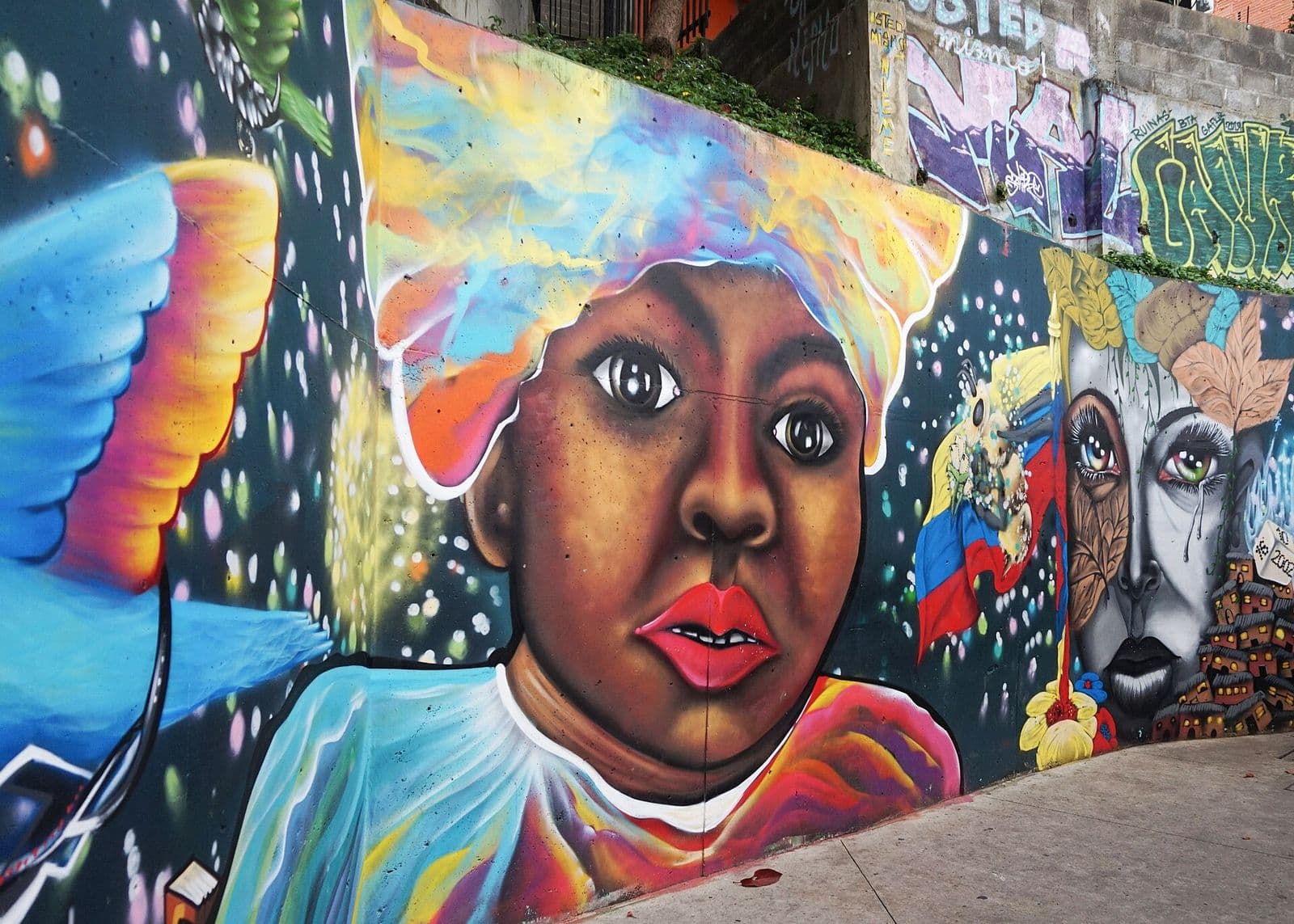 Vivid mural of an Afro-Colombian woman beside a rainbow hummingbird on a Comuna 13 wall