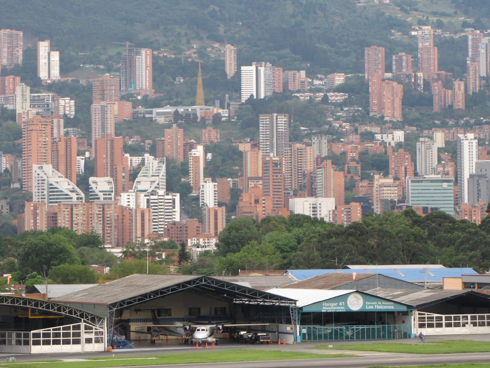 Terracotta high-rises of El Poblado climbing the green eastern hillside above Olaya Herrera airport