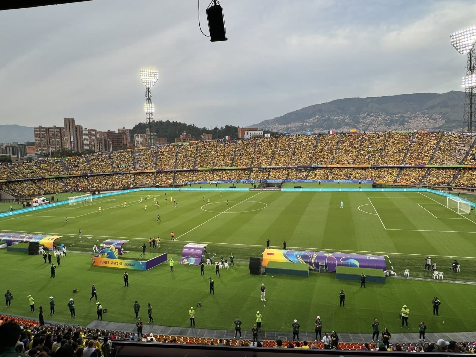 Tribunas llenas del Estadio Atanasio Girardot bajo los reflectores, con las montañas de Medellín detrás de la cancha