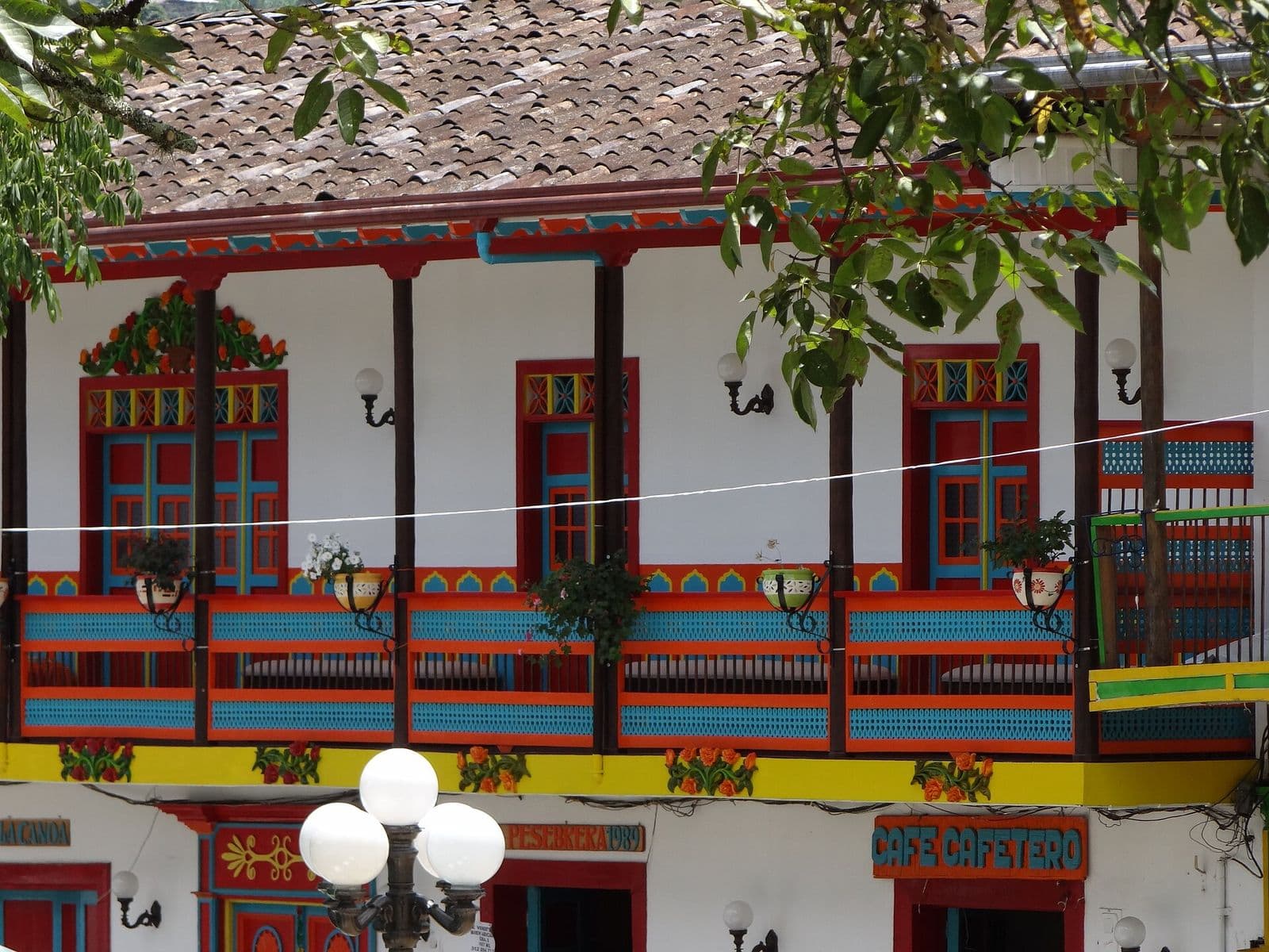 Ornate red, yellow and green wooden balconies on a colonial house facing Jardín's main plaza