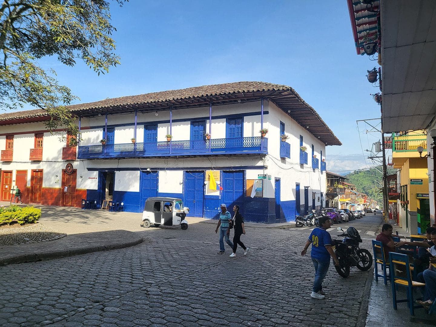 Blue-and-white colonial house on the sunny cobbled plaza of Jardín, Antioquia, with mountains behind