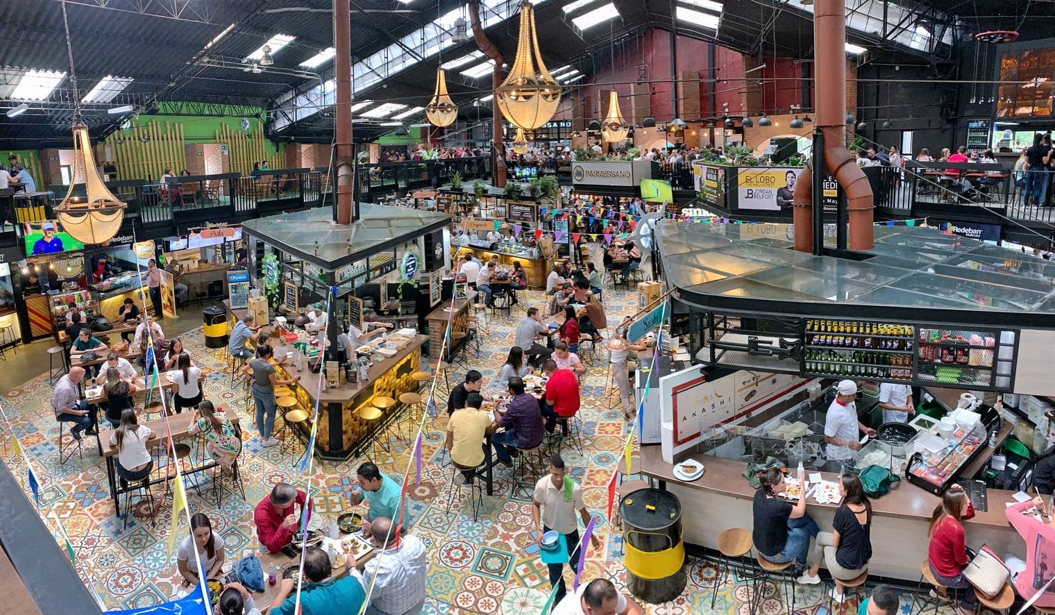 Bustling Mercado del Río food hall with patterned tile floors, chandeliers and busy food stalls