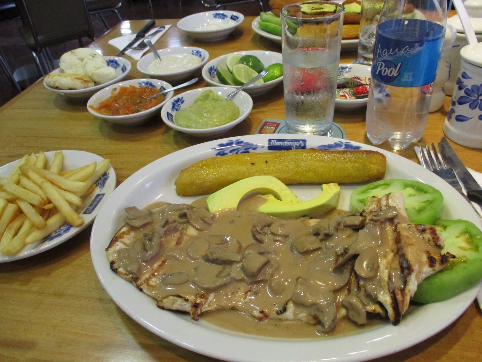 Carne asada en salsa de champiñones con plátano, aguacate y papas fritas en un plato con la marca Mondongo's