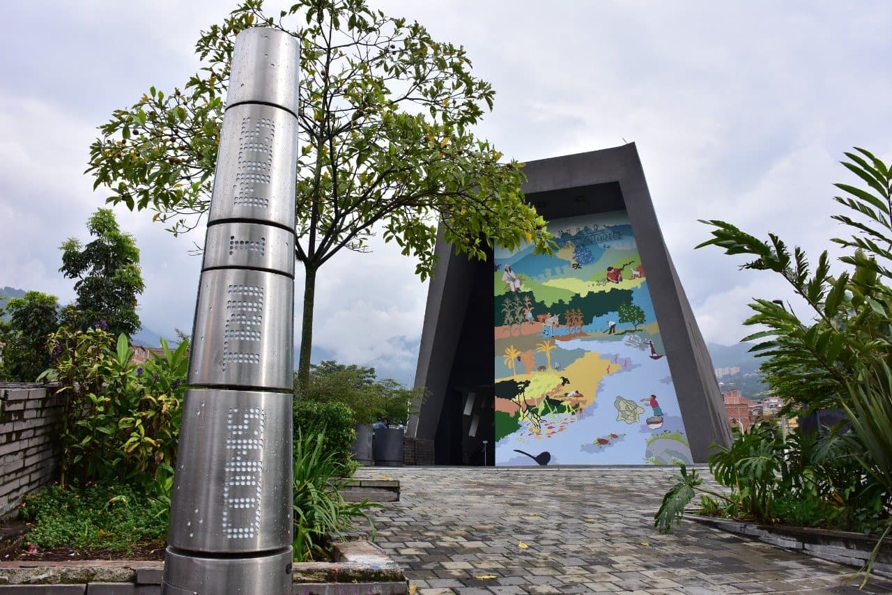 Angular dark facade and painted mural of the Museo Casa de la Memoria amid garden greenery