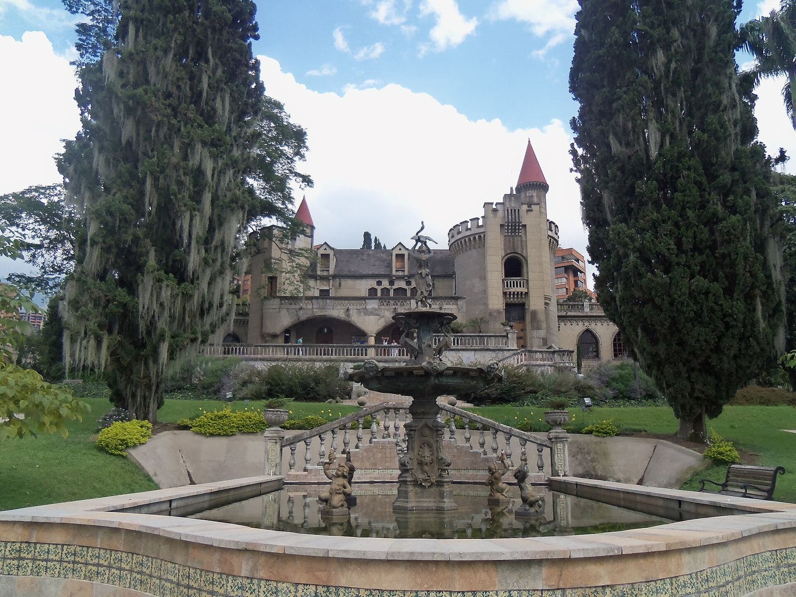 Museo El Castillo enmarcado por altos cipreses detrás de una fuente en sus jardines