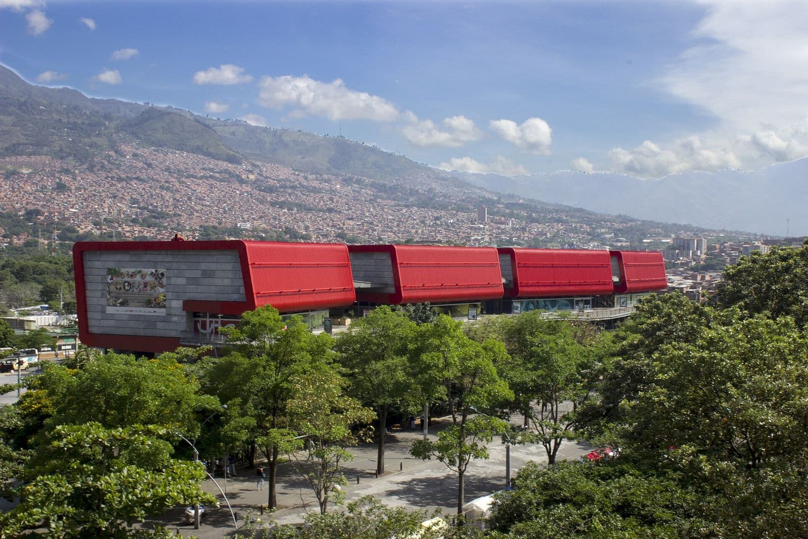 Los cubos rojos del Parque Explora sobresaliendo entre los árboles, con las montañas del norte de Medellín al fondo