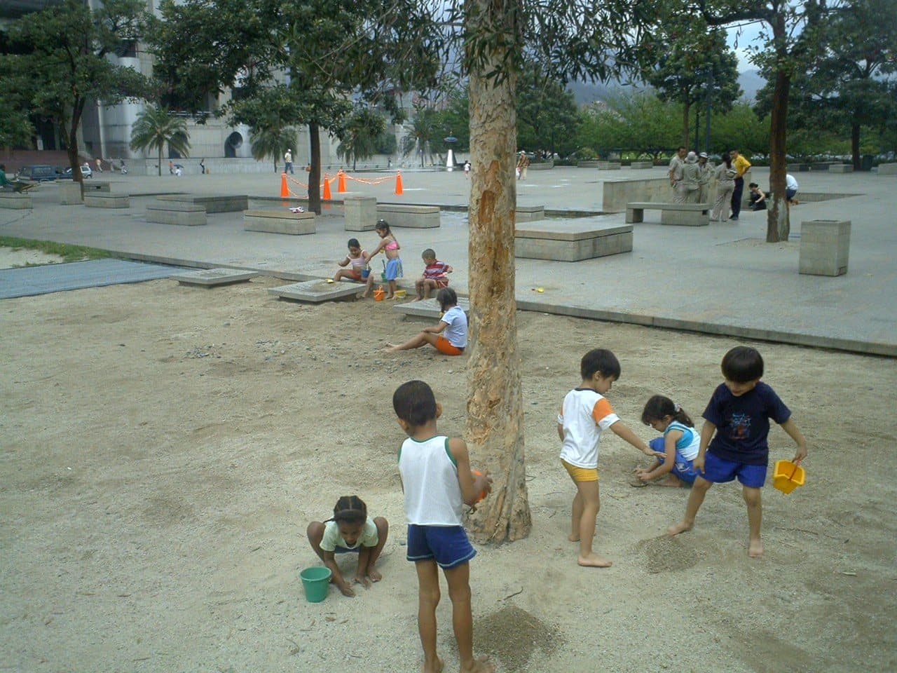 Children playing barefoot in the sand under tall trees at Parque de los Pies Descalzos