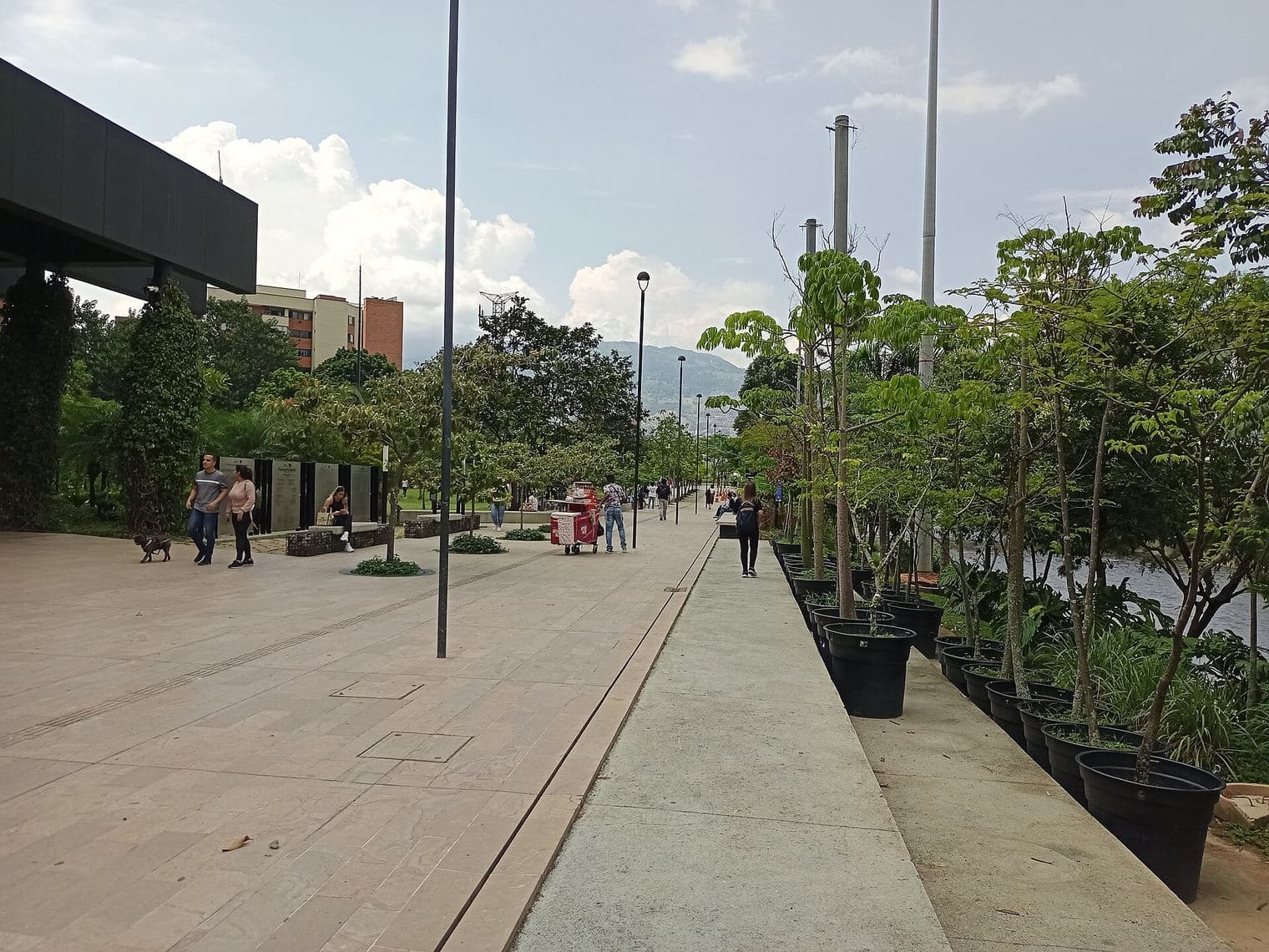 Amplio paseo arborizado con jardineras a lo largo de Parques del Río en un día despejado en Medellín