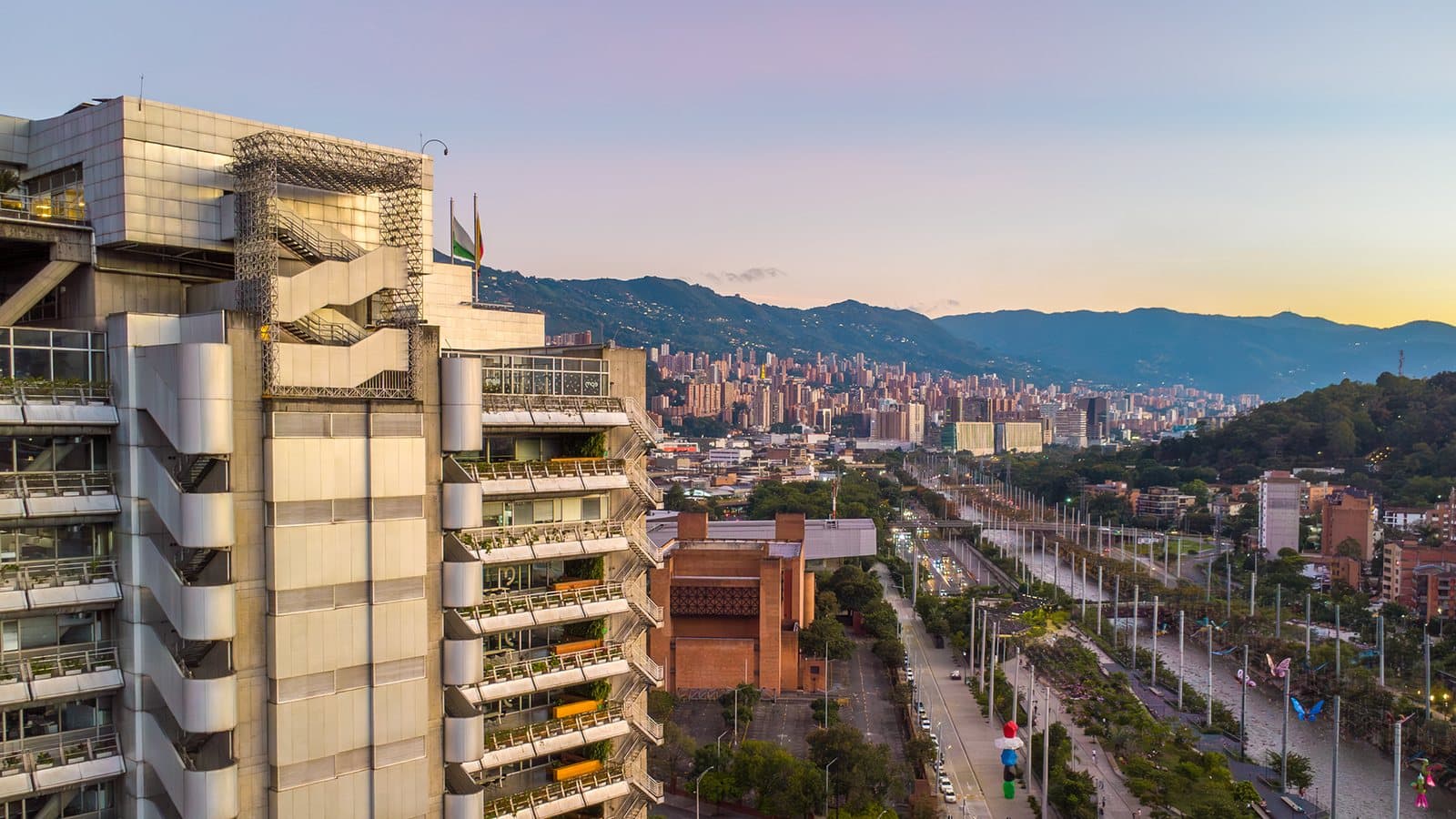 Vista a la hora dorada del corredor verde junto al río de Parques del Río, con el horizonte y las montañas de Medellín