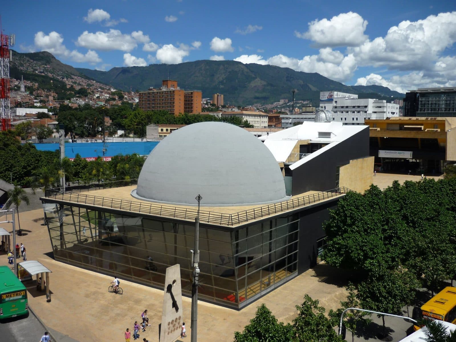 The grey dome of the Planetario de Medellín beneath billowing white clouds and green mountains