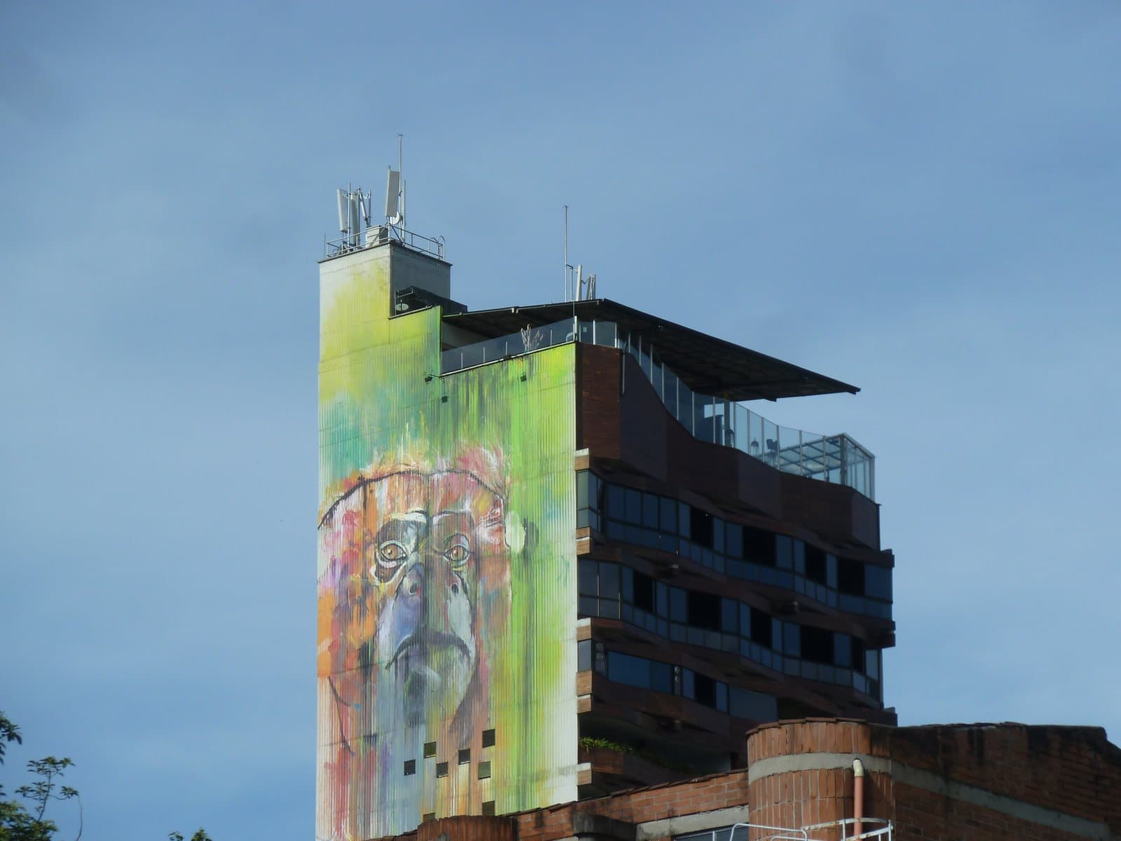 Towering painted mural on a building corner above the leafy streets of Provenza under evening sky