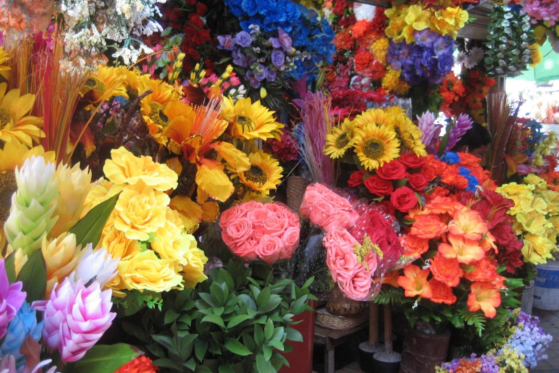Ramos vibrantes de flores amarillas, rosadas, naranjas y moradas apilados en un concurrido puesto de mercado