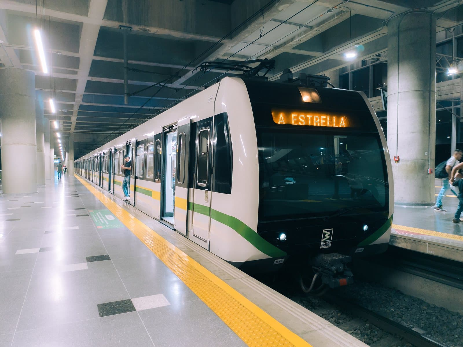 A white and green Medellín Metro train waits at a bright, spotless station platform