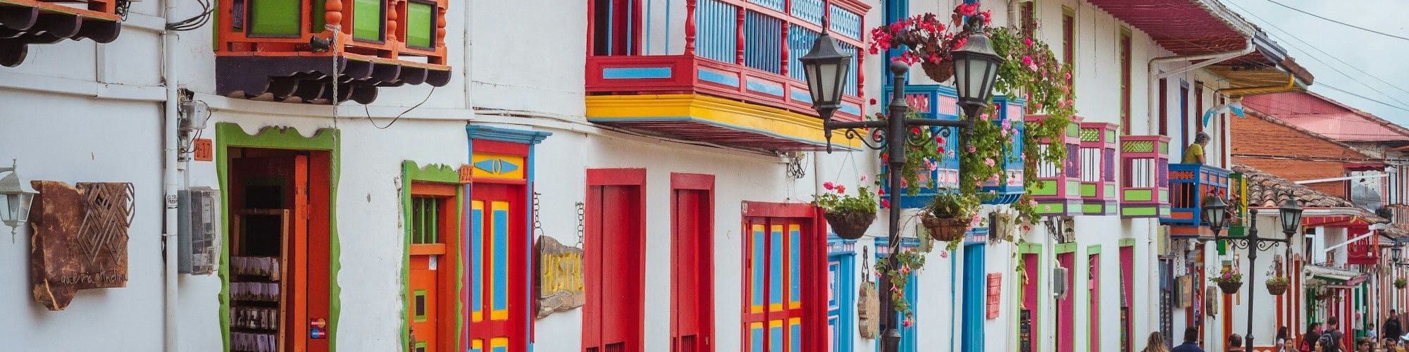 Rainbow-painted balconies and doors line a cobbled street in a Colombian coffee town