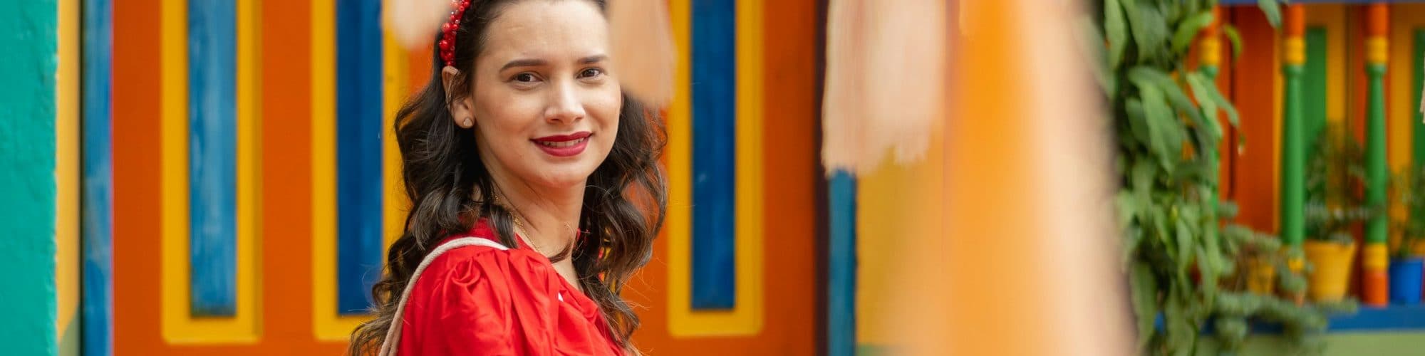 A smiling woman in red stands before a wall of bright painted stripes