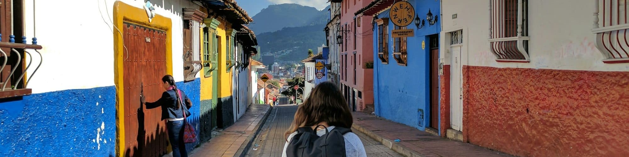 A traveler walks up a steep street of blue, yellow and red houses
