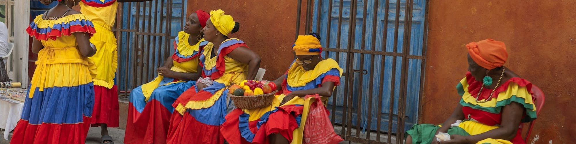 Palenqueras in red, yellow and blue dresses rest along a colorful Cartagena street