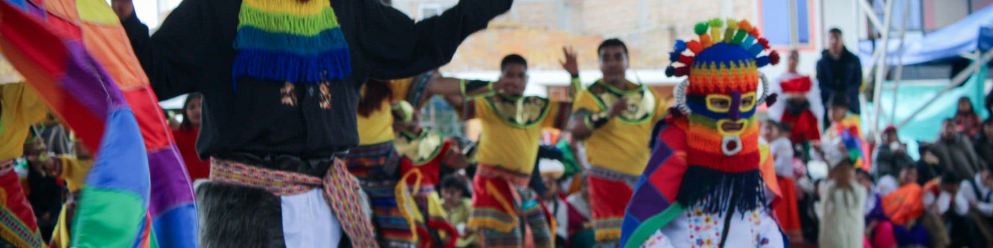 Dancers in masks and rainbow costumes fill the street during a Colombian carnival