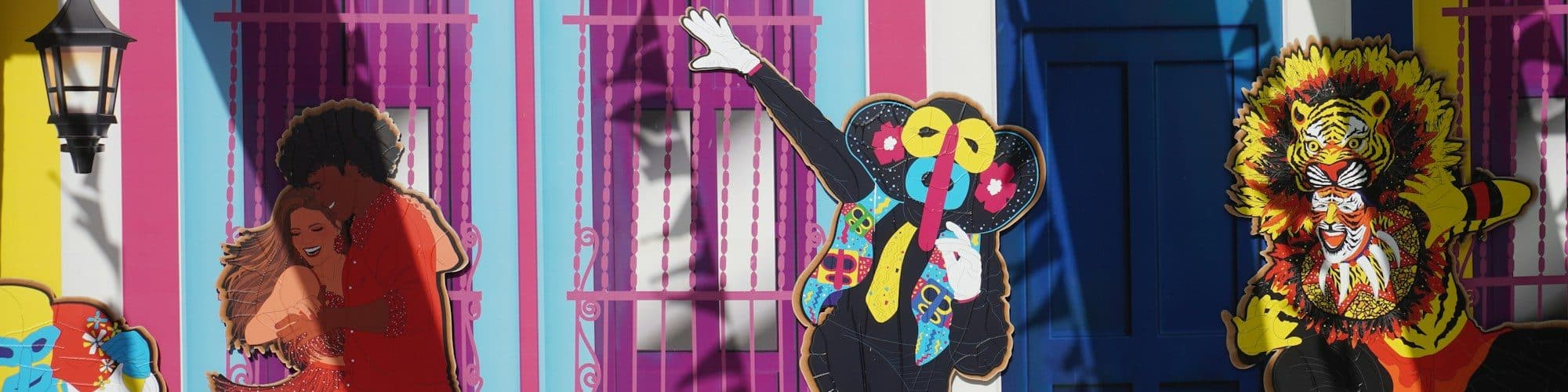 A vivid street mural of masks and carnival figures in pink, blue and yellow